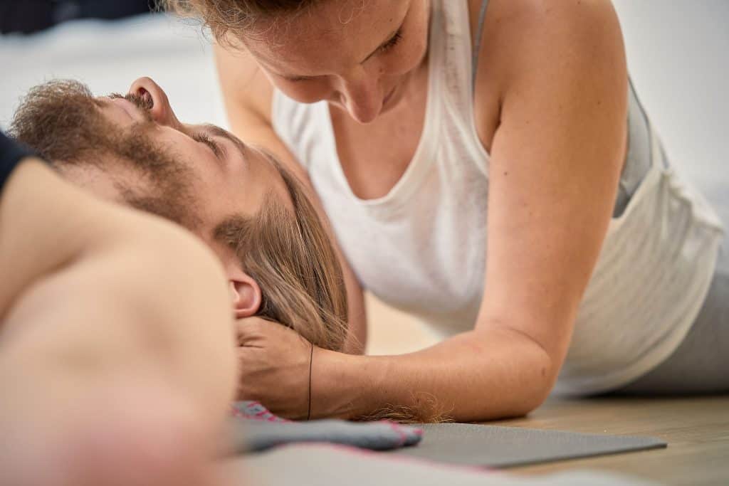 Frau im Liegen gibt Mann Craniosacral Arbeit am Kopf